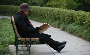 There is a man sitting on the table to read the book in the park.